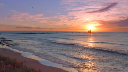 Wall Mural - Slow motion, graceful seagulls fly along shore at sunrise, with lighthouse in background
