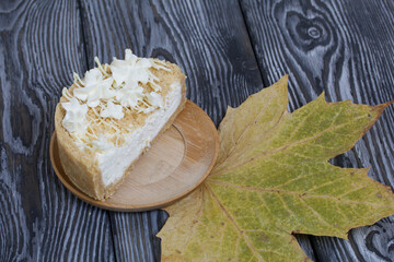 Cheesecake with white chocolate. The filling is visible on the cut. Nearby are dried maple leaves. On pine planks painted black and white.