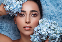 Creative Fashion Beauty Portrait Of Beautiful Young Woman With Blue Flowers Near Face.