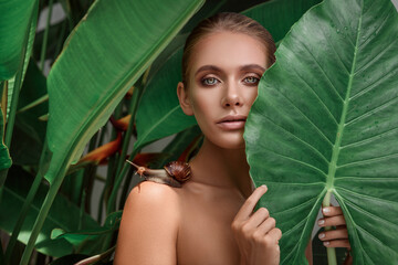 beautiful woman with snail on her shoulder. portrait pretty lady in a tropical leaves. concept spa a