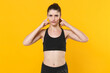 © ViDi Studio - Displeased young fitness sporty woman 20s wearing black sportswear posing training working out covering ears with fingers looking camera isolated on bright yellow color background studio portrait.