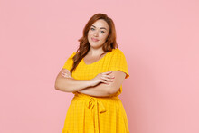 Smiling Beautiful Young Redhead Plus Size Body Positive Female Woman Girl 20s In Yellow Dress Posing Holding Hands Crossed Looking Camera Isolated On Pastel Pink Color Wall Background Studio Portrait.
