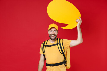 Wall Mural - Delivery employee man guy male in yellow cap t-shirt uniform thermal food bag backpack work courier service during quarantine coronavirus covid-19 hold speech bubble isolated on red background studio.