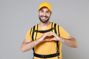 Wall Mural - Delivery employee man guy male 20s in yellow cap t-shirt uniform thermal food bag backpack work courier service during quarantine coronavirus covid-19 virus, posing isolated on gray background studio.