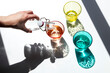 © Cavan Images - A person pours water into colored glass cups under the strong sunlight