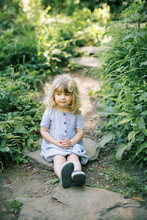 A Little Girl Sitting On A Stone Step Looking Over A River