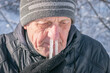 Comic concept of a winter cold. Portrait of an elderly man with icicles in his nose. The man's snot was frozen in his nose. Runny nose in the winter forest. Frosty weather in winter.