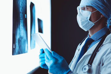 Doctor in hospital sitting at desk looking at x-rays on tablet against white background with x-rays