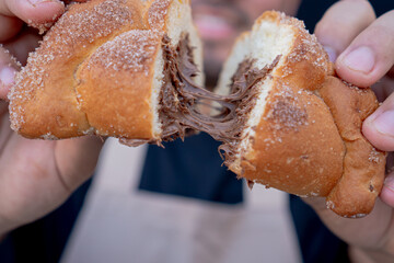 Delicious traditional Mexican pan de muerto or bread or dead stuffed with chocolate, broken in half by two hands.