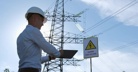 Wall Mural - a power engineer works on a tablet against the background of a power line metal pole, checking the s