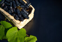 Black Ladies Finger Grapes In A Wicker Basket With Grape Leaves On A Black Background. Selective Focus. 