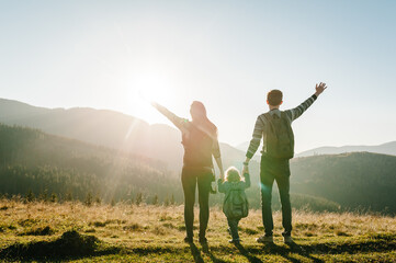 Mom, dad and daughter in the mountains enjoy sunset and look at nature. Back view. Young family spending time together on vacation, outdoors. The concept of family autumn holiday.