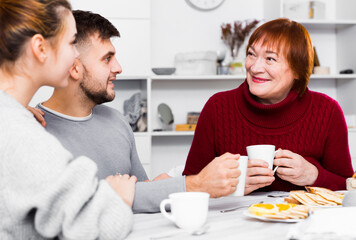 Wall Mural - Senior woman with young couple enjoying time at home, drinking tea with sweets