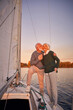 Sailing at sunset. Full length of happy senior couple holding hands and hugging while standing on the side of yacht deck floating in sea, man kissing his wife