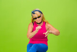 Fototapeta Młodzieżowe - Red manicure. Senior woman in ultra trendy attire isolated on bright green background. Looks stylish and fashionable, forever young. Caucasian mature woman in sunglasses, bright attire and sneakers.