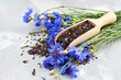 Black tea mix with dried cornflower petals and thyme in wooden scoop, fresh cornflowers bouquet.