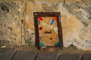 Installation of beautiful tiny wooden handmade door with decoration and mail sign on a limestone wall background.