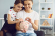 © Studio Romantic - Happy young mother and her lovely daughter putting coins into piggybank together at home, copy space text