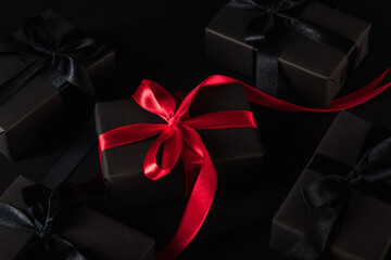 Black Friday sale shopping concept, Top view of gift box wrapped black paper and black bow ribbon present around the box with a red ribbon, studio shot on dark background