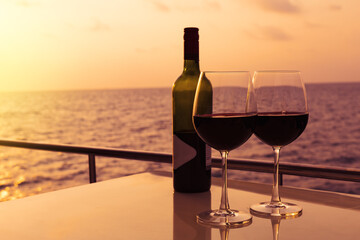 Glasses, red wine and tropical sunset with sea background, nobody.