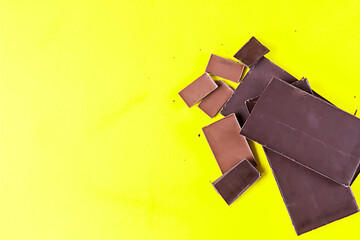 Dark and milk chocolate on pastel yellow background. Top view. Copy space.