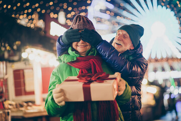 Wall Mural - Photo of two people retired lovers couple palms closing eyes curious grandma wait unbox newyear giftbox wear mittens coat red scarf headwear x-mas evening street park lights fair outside