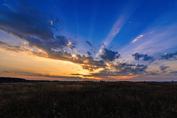 Wall Mural - orange blue sunset with sun rays through the clouds in the sky in the field in the evening