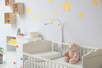 Poster - Crib with toy bear and mobile in stylish baby room interior