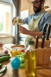 © Svitlana - Young man, Italian cook pouring white wine into the glass while preparing a meal in the kitchen