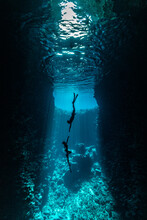 A Couple Of Freedivers Handing Diving In The Cave With Sun Rays