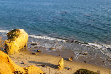 a shot of the deep blue ocean and the waves rolling into the beach with people relaxing on the beachat El Matador beach in Malibu California