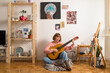 © mihajlo ckovric/Stocksy - Young woman playing guitar at home