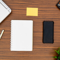 An office table working enviroment. Notepad, sticky note, pen plant, calculator and a lap top on a brown striped zebrawood design table top. Must have objects while working from home during Covid-19