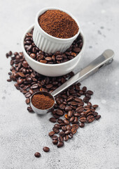 Fresh raw organic coffee beans in white bowl and powder on ligh background with round steel scoop.