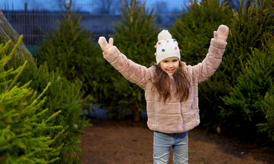 Poster - winter holidays and people concept - happy smiling little girl over christmas trees at street market in evening