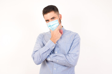 Sticker - Portrait of thoughtful smiling man keeps hand under chin, looks directly at camera, listens something with interest, dressed casually, poses against gray wall. Youth concept.