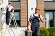 © LIGHTFIELD STUDIOS - Selective focus of builder in uniform with toolbox showing ok gesture while colleague working near building