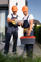 Wall Mural - Selective focus of builders with tool belt and toolbox using digital tablet on urban street