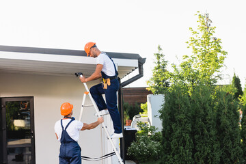 Wall Mural - Builders using ladder near facade and roof of building on urban street