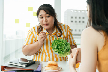 Wall Mural - Fat woman try to eat healthy salad for lunch in office room.