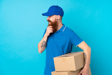 Redhead delivery man over isolated blue background thinking an idea and looking side