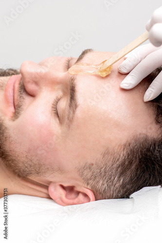 Beautician applies wax between male eyebrows before the procedure of waxing in the beauty salon.