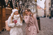 © Ivan - Two friends while shopping in knitted mittens, walking in the market square decorated with garlands on a winter day. Enjoy the winter festive mood.