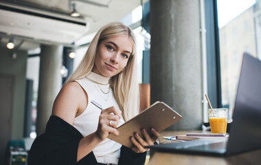 Positive businesswoman writing on clipboard with pen