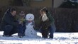 © MEDIAIMAG - Happy family building a snowman together, child baby brother and young parents outdoor, winter holiday