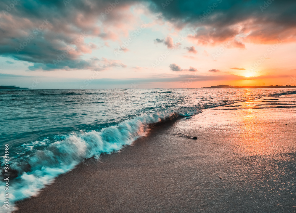 Ocean sunset, waves washing in over the sand. Strong sunset colors and clouds over the horizon - obrazy, fototapety, plakaty 
