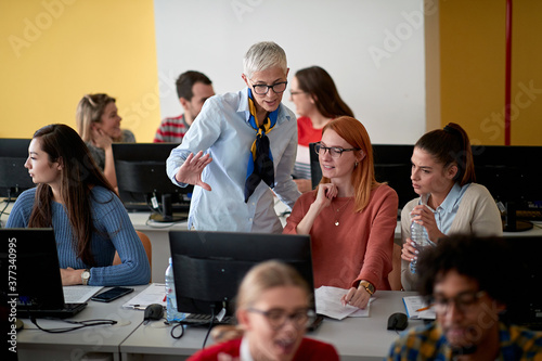 Female professor inspecting the work of students at an informatics lecture