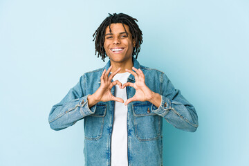 Young black man wearing a jeans jacket smiling and showing a heart shape with hands.