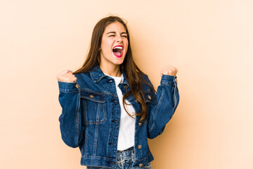 Wall Mural - Young caucasian woman isolated en beige background raising fist after a victory, winner concept.