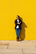 © Cavan Images - Young bearded man standing against a yellow wall with crossed arms